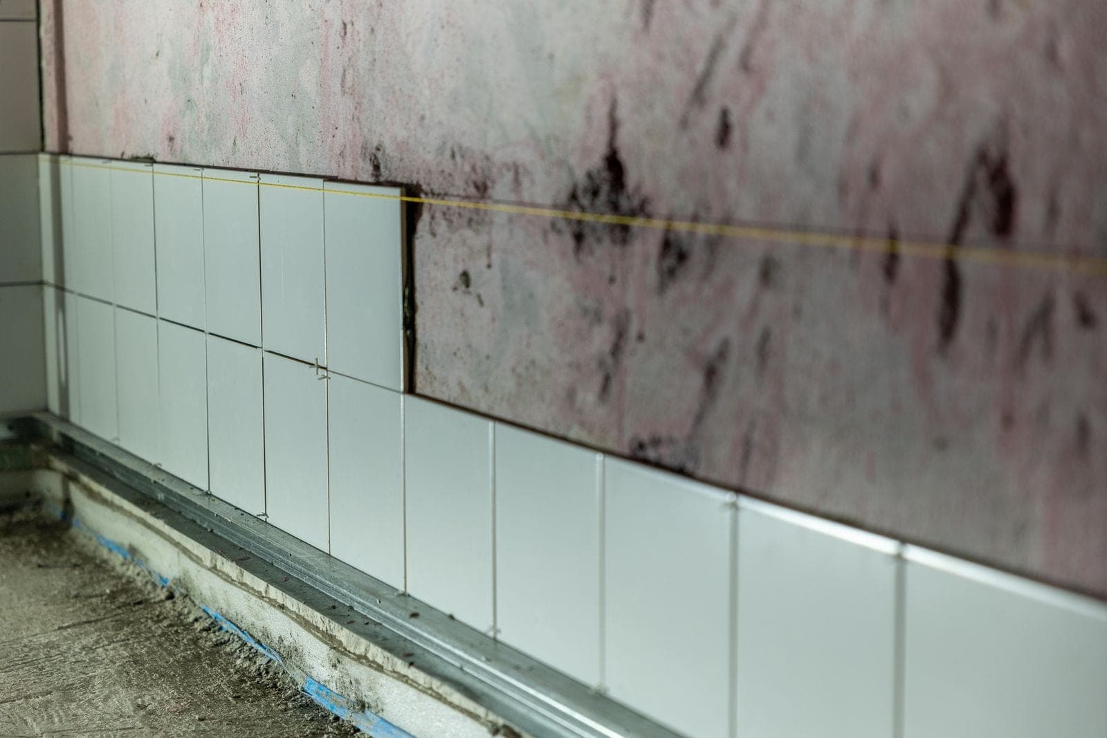 White wall tile being pulled off a bathroom wall during a remodel